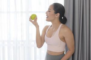 caber jovem comendo uma maçã depois de trabalhar em casa, esporte e conceito de estilo de vida saudável. foto