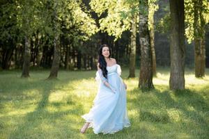 mulher grávida de chapéu posando em um vestido em um fundo de árvores verdes. foto