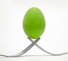 um ovo de galinha verde é colocado na ponta de um talher em um fundo branco. foto
