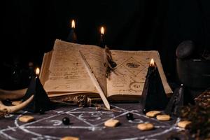abra o livro antigo com feitiços mágicos, runas, velas pretas na mesa de bruxa. conceito oculto, esotérico, adivinhação e wicca. foto