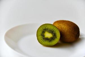 um kiwi inteiro e metade em um prato branco foto