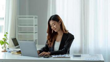 encantadora empresária asiática sentada trabalhando no laptop no escritório. foto