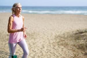 mulher madura correndo ao longo da costa da praia. mulher mais velha fazendo esporte para manter a forma foto