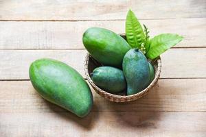 frutas de verão manga verde e folhas verdes na cesta em fundo de madeira - manga crua fresca foto