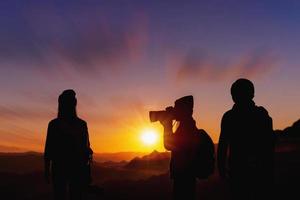 jovem fotógrafo tirando foto de seu amigo com pôr do sol no fundo natural da montanha.