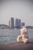 um ursinho de pelúcia marrom fofo senta-se em uma única ponte com vista para o mar com um fundo de espaço de cópia. solitário, a solidão é inútil. foto