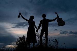 silhueta de um casal apaixonado em um encontro. o homem segura a mão da garota. o cara em caranguejos tem uma guitarra. filmado ao pôr do sol. foto