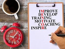 melhorar, desenvolver, treinar, motivar, treinar, inspirar o texto do mentor escrito à mão na área de transferência e despertador vermelho e café na mesa de madeira