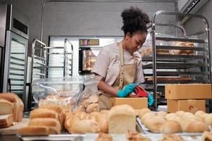 entrega de pequenas empresas de inicialização de padaria. uma cozinheira afro-americana está embalando pães e doces feitos à mão e recém-assados em caixas e enviando para compras on-line de clientes na cozinha culinária. foto