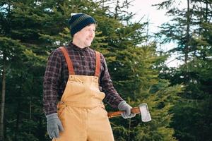 homem lenhador com um machado nas mãos em um fundo de floresta e árvores foto