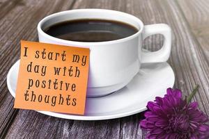 citação motivacional escrita na nota da vara com xícara de café branca e flor roxa foto