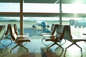 assento da sala de embarque do aeroporto com aeronave se preparando para o voo em segundo plano foto