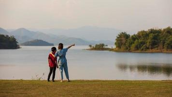 mãe e filho ao lado do grande lago e ver a vista para a montanha ao fundo, mãe apontando o dedo para a floresta. ideia para viagens turísticas em família juntas para a viagem ao ar livre foto