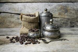 xícara de prata e grãos de café em saco de saco em fundo de madeira foto