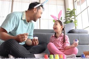 filha pai preparar lindos ovos de páscoa para decoração e celebração início da primavera, adorável coelhinho rosa criança e seu pai com cabeça de orelhas de coelho pintando ovos coloridos juntos. foto