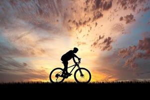 silhueta de um ciclista em um belo prado à noite. ideias de férias de bicicleta foto