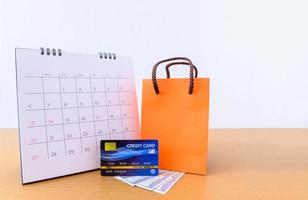 calendário com dias e cartão de crédito e saco de papel laranja na mesa de madeira. conceito de compras foto