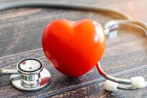 coração vermelho, estetoscópio e família de ícones na mesa de madeira. conceito de seguro médico foto