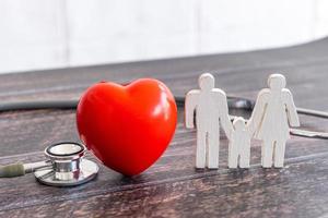 coração vermelho, estetoscópio e família de ícones na mesa de madeira. conceito de seguro médico foto