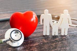 coração vermelho, estetoscópio e família de ícones na mesa de madeira. conceito de seguro médico foto