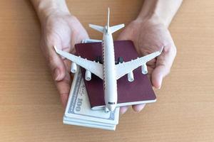 mãos de homem segurando notas de 100 dólares e avião na mesa de madeira. conceito de viagem foto