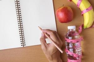 conceito de alimentação saudável, fita métrica, frutas e garrafa de água em um fundo de madeira, caderno de espaço de cópia em branco foto