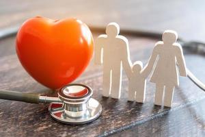 coração vermelho, estetoscópio e família de ícones na mesa de madeira. conceito de seguro médico foto