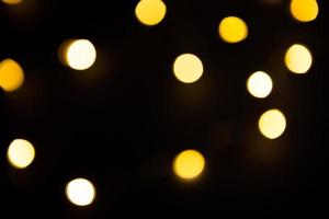 guirlanda de luzes amarelas e douradas em um borrão em um fundo preto. bokeh de círculos voadores na desfocagem. atmosfera festiva de natal e ano novo. celebrar o fundo foto