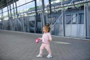 uma menina tenta andar sozinha no contexto de um edifício moderno. na mão de uma garota segurando um copo de derramamento. foto