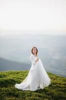 mulher em um vestido de noiva atravessa o campo em direção às montanhas
