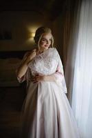 uma jovem noiva loira bonita em um roupão de banho está experimentando seu vestido de noiva. foto