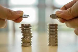 conceito de negócios, economia e aposentadoria. close-up da mão de dois homens segurando a moeda e colocando em cima de duas pilhas de moedas na mesa de madeira. foto