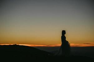 mulher em um vestido de noiva atravessa o campo em direção às montanhas foto