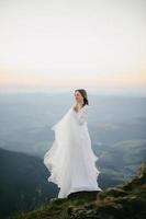 mulher em um vestido de noiva atravessa o campo em direção às montanhas foto