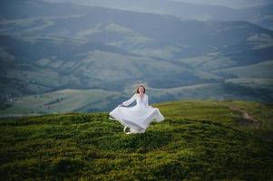 mulher em um vestido de noiva atravessa o campo em direção às montanhas foto