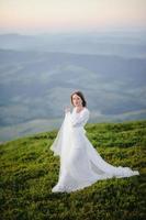 mulher em um vestido de noiva atravessa o campo em direção às montanhas