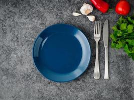 limpe o prato escuro azul vazio, garfo e faca no fundo cinza de concreto, vista superior. foto