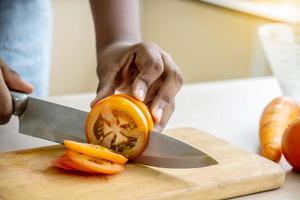 close-up de mão garota afro-americana cortando tomates na tábua com faca na cozinha foto