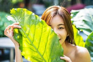 retrato de uma bela jovem asiática com maquiagem natural detém uma grande folha verde sobre um fundo verde turva. spa e bem-estar. juventude, adolescentes e conceito de cuidados com a pele foto