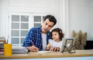 jovem pai atraente e filha bonita assistindo o tutorial em vídeo no tablet e ensinando lição de casa em casa com felicidade. foto