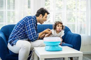 mão pai rolando algodão doce na máquina de algodão doce e comer algodão doce junto com a filha no sofá em casa nova foto