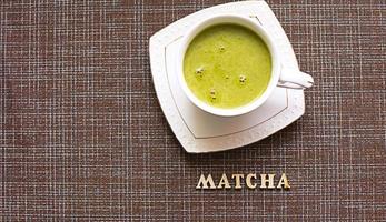 chá verde matcha japonês é derramado em uma caneca branca e em um pires branco em pó. inscrição em letras de madeira em inglês. jogo de chá, bebida revigorante, vigor, antioxidante. espaço para texto foto