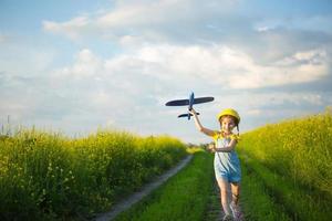 garota de chapéu panamá amarelo lança um avião de brinquedo para o campo. horário de verão, infância, sonhos e descuido. tour aéreo de uma agência de viagens em uma viagem, aventura e férias. aldeia, núcleo de casa de campo foto