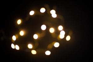 guirlanda de luzes amarelas e douradas em um borrão em um fundo preto. bokeh de círculos voadores na desfocagem. atmosfera festiva de natal e ano novo. celebrar o fundo foto