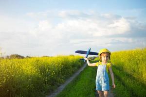 garota de chapéu panamá amarelo lança um avião de brinquedo para o campo. horário de verão, infância, sonhos e descuido. tour aéreo de uma agência de viagens em uma viagem, aventura e férias. aldeia, núcleo de casa de campo foto