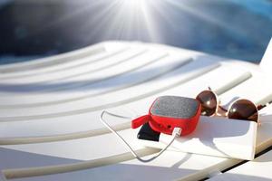 o alto-falante portátil red music é carregado pelo banco de potência via usb em uma espreguiçadeira perto da piscina. conceito está sempre em contato, gadgets de viagem, bateria externa para smartphone. lugar para texto. flatlay foto