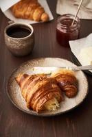 café da manhã com croissant no prato, xícara de café, geléia e manteiga. vertical, vista lateral