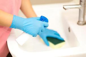 pessoa, uma mão em uma luva de borracha azul na foto, remove e lava a pia do banheiro foto