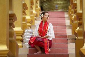 jovem asiática em traje tradicional birmanês, segurando a tigela de arroz na mão no pagode dourado no templo de mianmar. mulheres de mianmar segurando flores com vestido tradicional birmanês visitando um templo budista foto