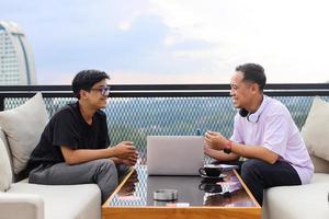 dois estudantes universitários asiáticos em discussão estudando juntos usando laptops no café foto